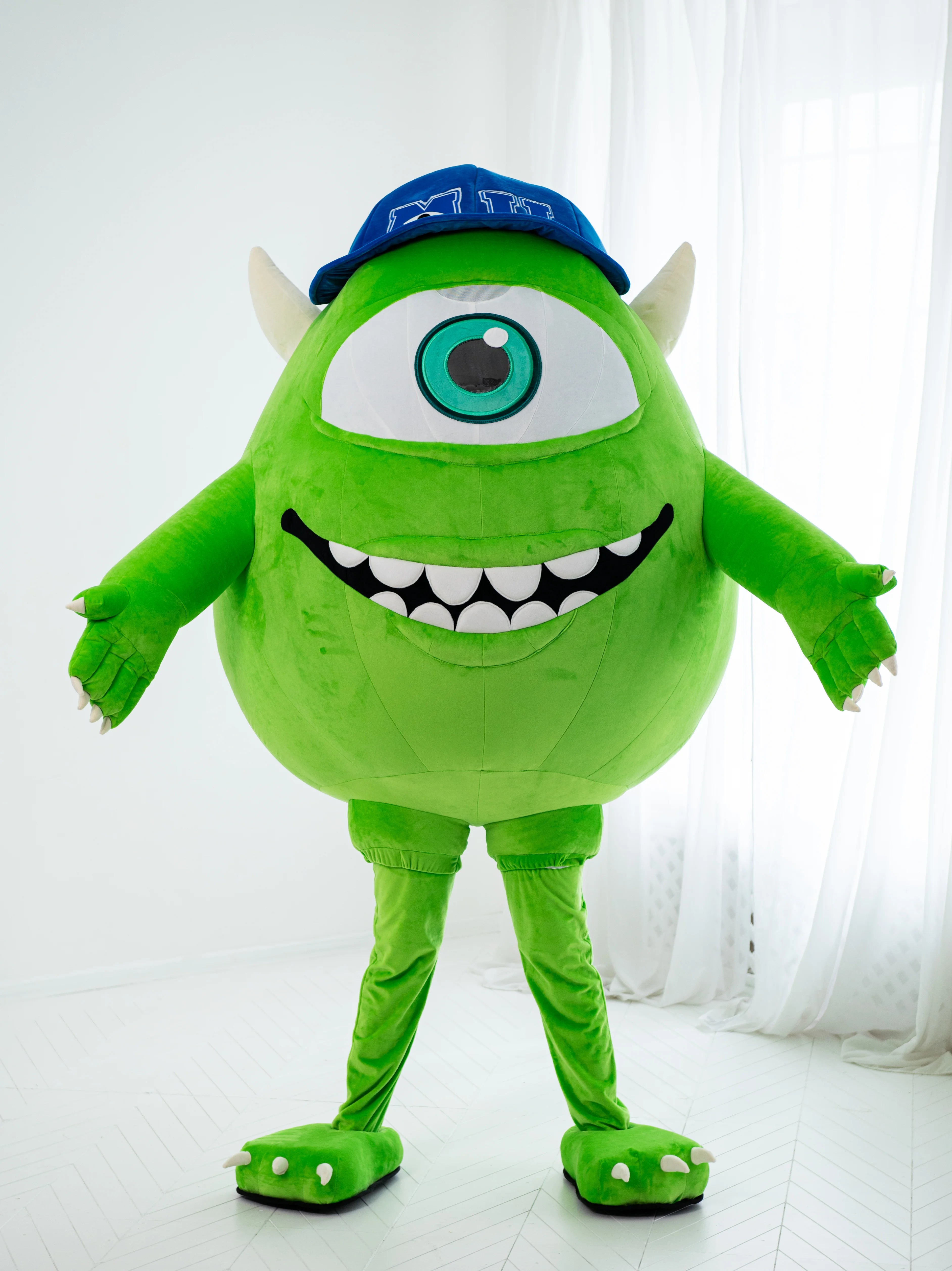 Green monster mascot costume with a blue cap on a white background