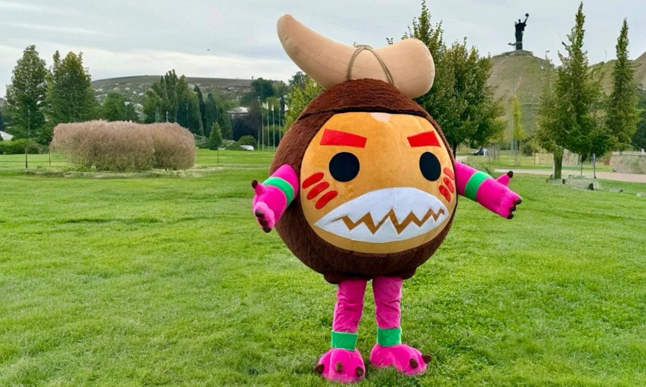 Person in a cartoonish bull mascot costume standing on grass with trees and a statue in the background